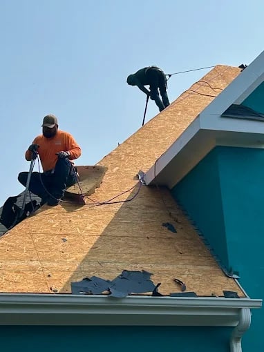 Workers installing wooden roof sheathing on a teal-colored house