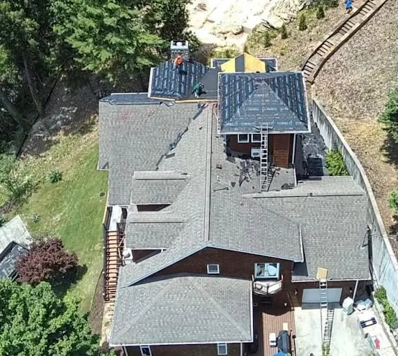 Aerial view of house with workers installing or repairing roof shingles