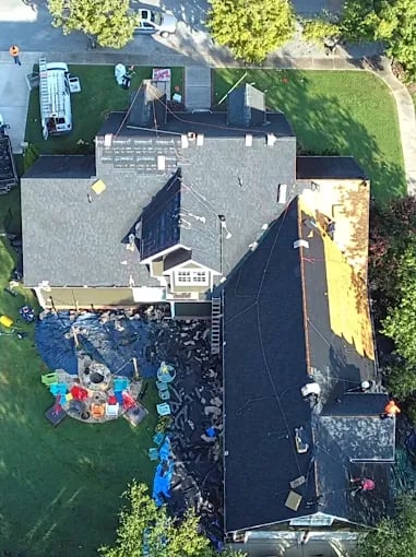 Aerial view of house roof repair with colorful tarps and construction materials
